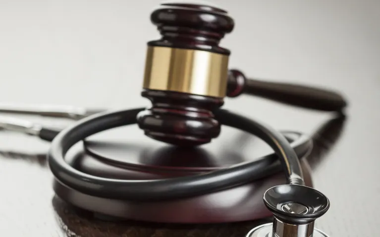 Dark wooden judge's gavel resting on a sound block, intertwined with a black stethoscope.