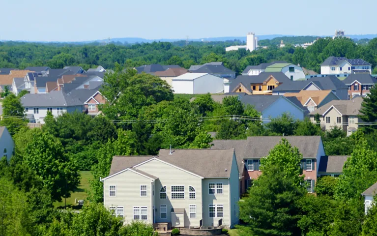 View of a suburban neighborhood with multiple houses surrounded by green trees under a clear blue sky.