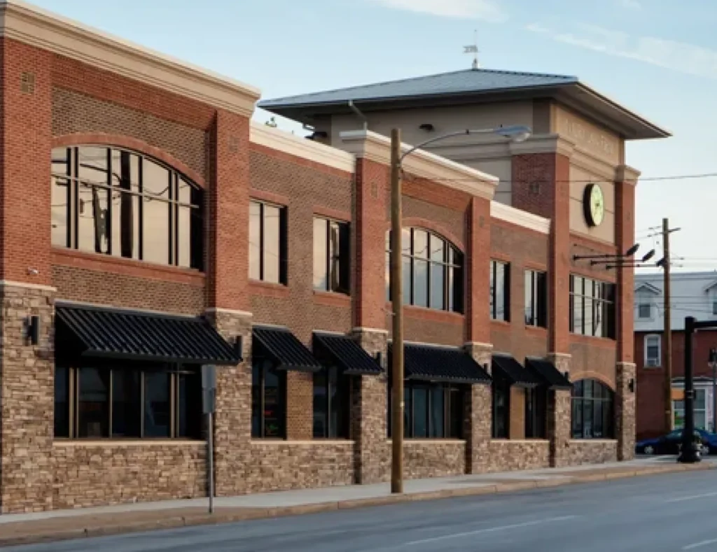 Two-story brick commercial building with large windows and black awnings, clock tower visible.