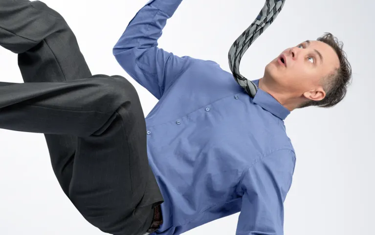 Man in blue shirt and black trousers appearing to fall, with tie flying upward.