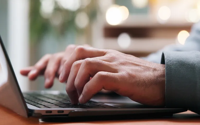 Close-up of adult hands typing on a black laptop keyboard in a softly lit indoor setting.