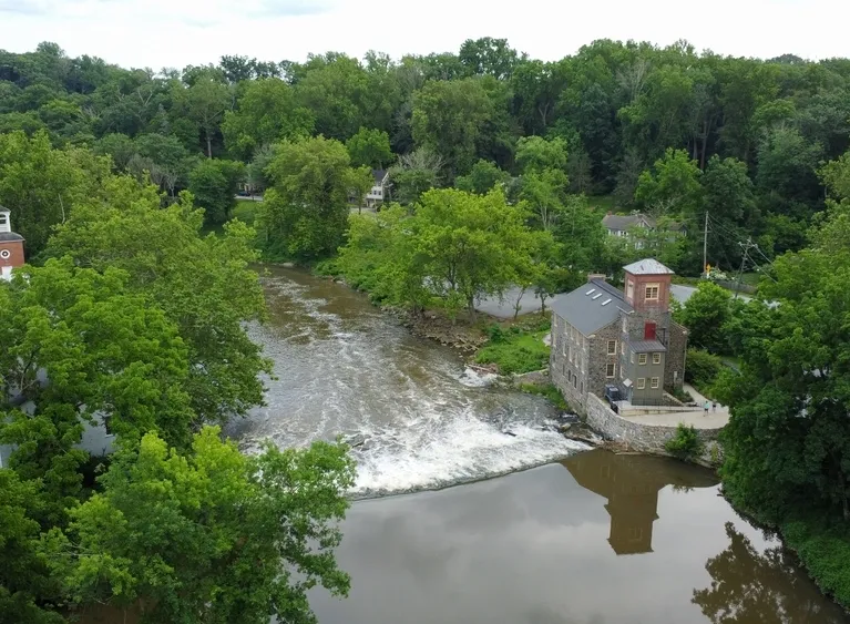 Aerial view of a historic stone building by a flowing river surrounded by dense green trees.